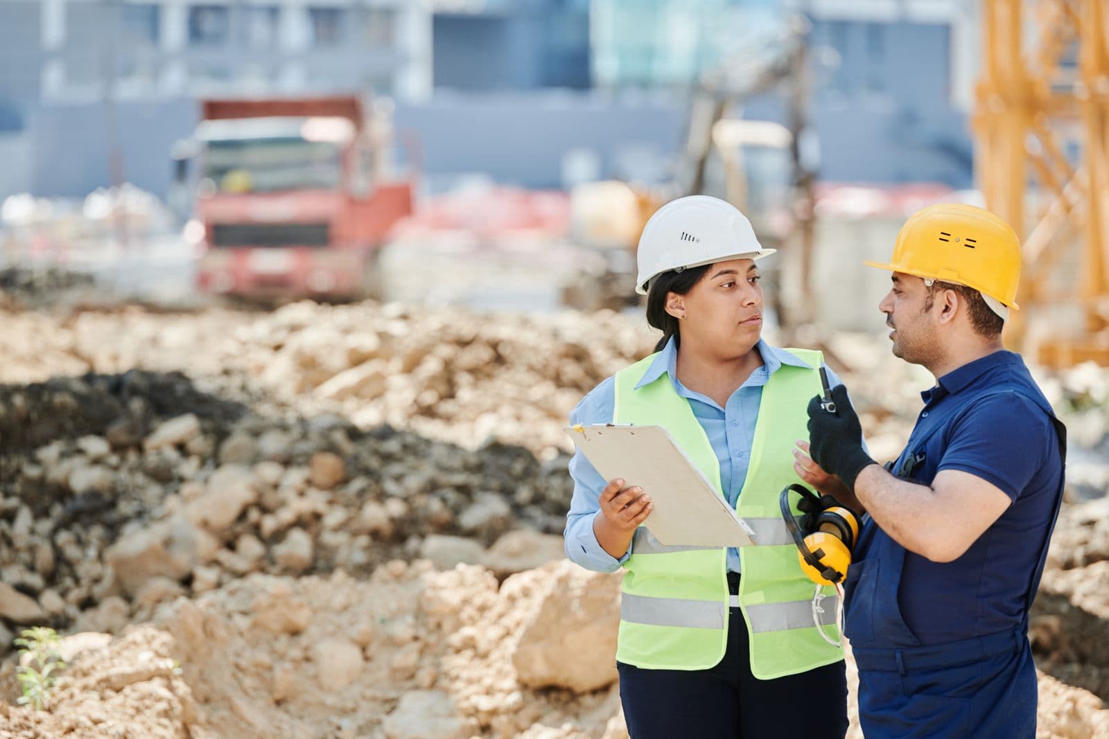 Two people in hard hats talking on a construction site